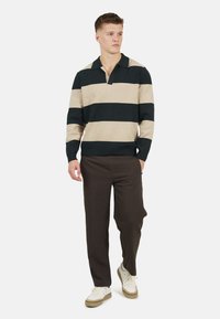 Pasiasty sweter w kremowo-granatowe pasy, z kołnierzykiem i długimi rękawami. Noszony z ciemnymi spodniami i białymi sneakersami. Gładka dzianinowa faktura.