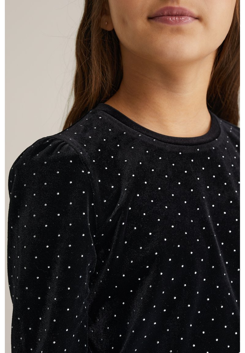 Fekete bársony felső ezüst pöttyös részletekkel, kerek nyakkivágással és puffos ujjakkal. A textúrája sima és puha, diszkrét csillogást kölcsönöz.