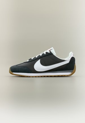 Baskets Nike noir et blanc avec lacets blancs et semelle en gomme, présentées en profil latéral sur un fond neutre.