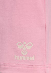 Chemise rose à manches courtes en tissu doux, présentant une texture côtelée subtile et un logo blanc en forme d'abeille près de l'ourlet.
