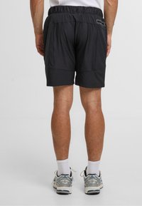 Manns svarte treningsshorts med elastisk midje. Har sidelommer og glatt stoff. Brukt med hvite sokker og joggesko.
