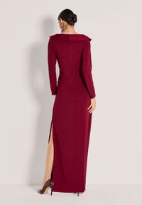 Bordeauxrotes Abendkleid mit langen Ärmeln, figurbetonter Silhouette, schulterfreiem Ausschnitt und Seitenschlitzen. Glatter Stoff und dezente Details.