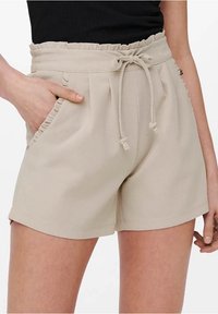 Pantaloni corti beige con vita elasticizzata a volant, cordoncino regolabile e tasche laterali. Realizzati in un tessuto morbido e leggero.