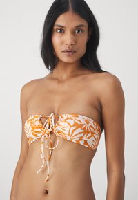 Top bikini bandeau floreale arancione e bianca con dettaglio a cravatta al centro. Tessuto morbido, texture liscia e design arricciato che aggiunge profondità.