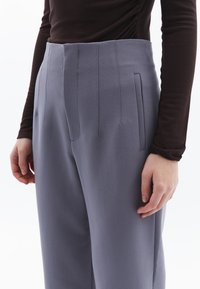 Grå skräddarsydda byxor med hög midja, med vertikala sömnadsdetaljer och sidofickor; tyget har en slät, matt textur.