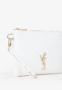 La pochette bianca trapuntata presenta una cerniera e accessori dorati, con una tracolla rimovibile e un logo in rilievo sul davanti. Texture liscia.