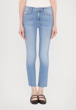 Jeans slim fit azzurri chiari con orli sfrangiati, indossati con ballerine nere a doppio cinturino e top bianco, mostrati dalla vita ai piedi.