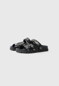 Μαύρα σανδάλια slide με δύο φαρδιές λουριά διακοσμημένα με χρυσές τρύπες, με υφή στη σόλα και ελαφριά, ογκώδη σχεδίαση.