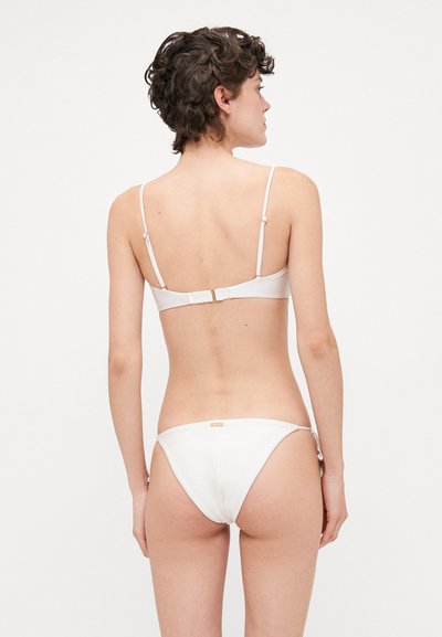 Hvid bikini sæt med justerbare tynde stropper, lukning med spænde i ryggen og enkelt design. Glat tekstur med minimal udsmykning.