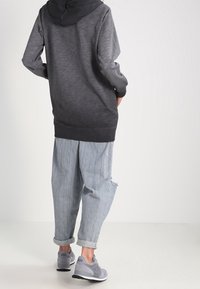 Felpa con cappuccio in gradiente nero e grigio, abbinata a jeans baggy chiari e strappati e sneakers grigie con logo.