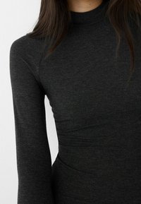 Mörkgrå, figurnära långärmad topp i ett mjukt, strukturerat material med hög halsringning och subtil detaljerad midja.
