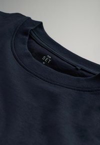 Navyblaues Baumwoll-T-Shirt mit Rundhalsausschnitt. Das Innenetikett trägt die Aufschrift "THE SET M." Glatte Textur mit minimalen Nähdetails.