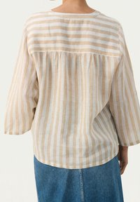 Top in lino a righe beige e bianco, con maniche a tre quarti, cucitura posteriore arricciata e scollatura rotonda.