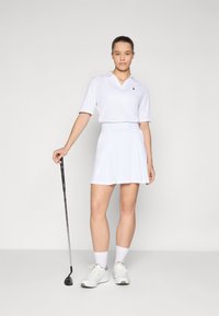 Hvid golf polo-shirt med korte ærmer, parret med en matchende hvid skorts. Hvite sportsko og et golfkølle er også inkluderet.