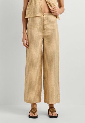 Beige, vertikal gestreifte, weit geschnittene Hose mit Knöpfen vorne, kombiniert mit einem passenden ärmellosen Top und braunen Sandalen.
