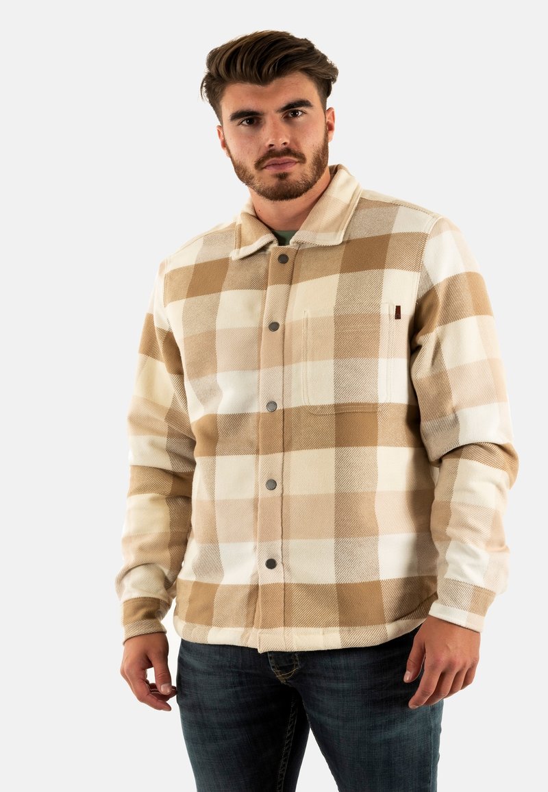 Tan en crèmekleurige geruite blazer met een kraag, een voorzak met flap en een textielstructuur, gedragen over een donkere jeans.