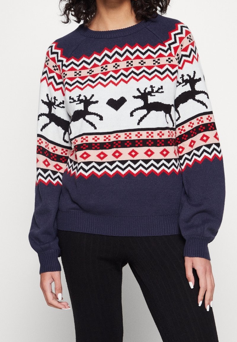 Marinblå tröja med röda och vita geometriska mönster, prydd med svarta renar och ett hjärtmotiv. Ribbad manschett och fåll, stickad struktur.