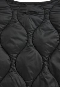 Czarna pikowana tkanina z falistym wzorem diamentowym i małą prostokątną metką z napisem "POLO CLUB" blisko środka górnej części.