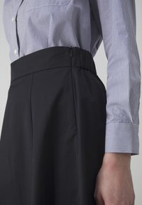 Černá sukně s vysokým pasem, který má skrytý zip a plisovaný design. V kombinaci s modro-bílou pruhovanou košilí.