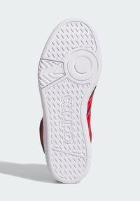 Czerwono-czarny but sportowy z teksturowaną białą gumową podeszwą, z okrągłym emblematem i zygzakowatym wzorem zapewniającym przyczepność.