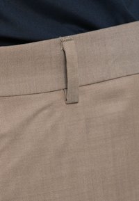 Μπεζ παντελόνι με επίπεδη υφή και διακριτό διαγώνιο ύφανση. Διαθέτει επίπεδο μπροστινό μέρος και μία ζώνη θηλιά στη μέση.