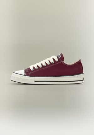 Baskets basses en toile bordeaux avec semelle en caoutchouc blanche, bout renforcé blanc et lacets blancs, vues de côté sur un fond neutre.