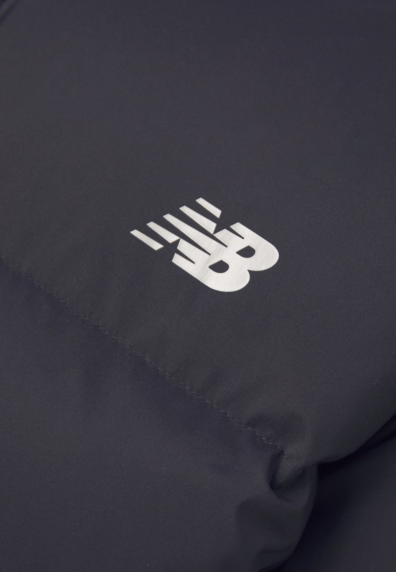 gepolsterte marineblaue Jacke mit einem hervorgehobenen silbernen Logo, das horizontale Linien und abgerundete Kanten aufweist, vor einer glatten Stofftextur.