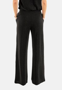 Pantalon large noir en tissu texturé, avec une taille haute et des poches latérales. Le matériau présente un léger éclat.