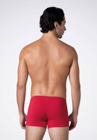 Boxer da uomo rossi realizzati in tessuto morbido, con una vestibilità aderente e un design semplice senza motivi o decorazioni visibili.