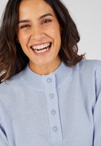 Lichtblauwe gebreide trui met een ronde kraag en een knoopsluiting met vier knopen. Zachte textuur met ribbelaccenten op de kraag en manchetten.