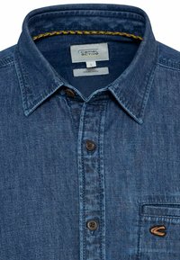 Denimskjorte i dyb blå med afslappet krave, front lukning med knapper, brystlomme og subtilt teksturmønster. Camel Active branding.