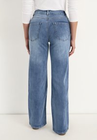 Vidbenade blå denimjeans med ljus tvätt, med bakfickor och en klassisk femfickdesign. Benänden är rent och jämnt avslutad.