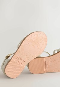 Glitter-covered sandals with a tan sole featuring a unicorn design. Straps are silver with a gold buckle. Textured, ribbed sole.