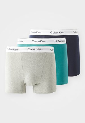 Tres pares de boxers para hombre en gris, verde azulado y marino. Todos tienen una cinturilla blanca con la marca "Calvin Klein". Material de algodón, diseño ajustado.