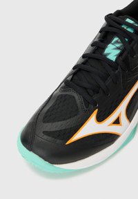 Black athletic shoe featuring a mesh upper, orange accent logo, turquoise sole, and black laces with a textured surface for grip.