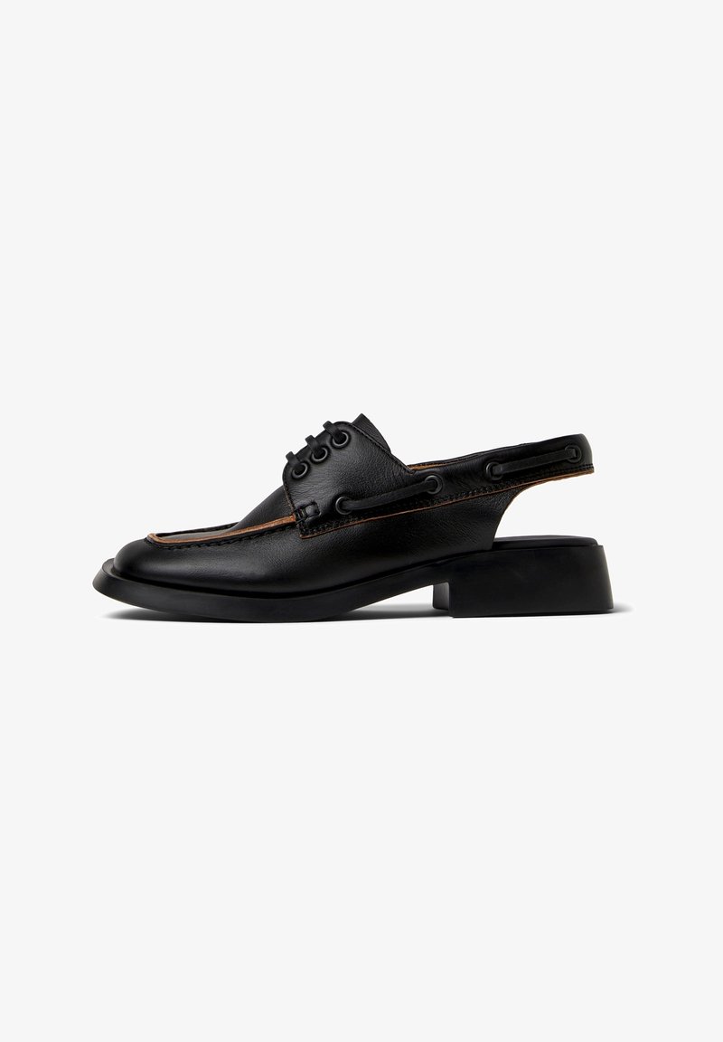 Mocassin à bride arrière en cuir noir avec petit talon bloc, couture moc toe, détail lacé, et bride arrière ouverte sur fond blanc.