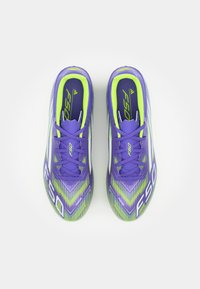 Des chaussures de football violettes avec un motif texturé agrémenté d'accents verts et blancs. Les caractéristiques incluent des lacets et une languette rembourrée pour le confort.