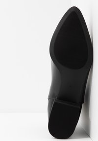 Chaussure en cuir noir avec un bout pointu, une tige lisse et une semelle en caoutchouc côtelée. Taille indiquée : 41. Présentée sur un fond blanc.