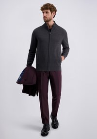 Kohlegrauer Reißverschluss-Pullover mit geripptem Kragen, kombiniert mit dunkelroten Hosen und schwarzen Schuhen, hält eine dunkelrote Jacke.