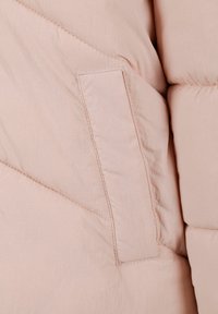 Svijetloružičasta puffer jakna od tkanine s glatkom teksturom, koja ima zakrpu na džepu i dijagonalno prošivenu chevron šemu.