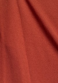 Gros plan d’un tissu orange rouille avec de fines côtes verticales et un pli doux créant une ombre.