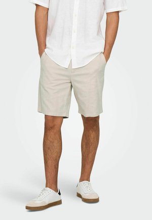 Shorts beige clair en tissu doux, dotés de poches latérales et d'une coupe droite, associés à des baskets blanches et une chemise blanche à manches courtes.