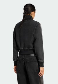 Crna kratka traper jakna s rebrastim ovratnikom i manžetama, s dvije pruge duž rukava. Nošena s odgovarajućim crnim traper hlačama.