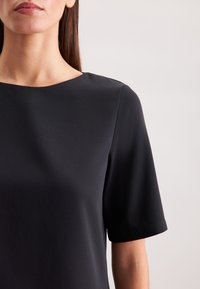 Top nero a maniche corte con scollatura rotonda, realizzato in tessuto liscio, caratterizzato da un design minimalista e una silhouette pulita.