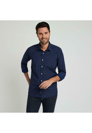 Chemise bleu marine à boutons avec un motif à pois subtil, manches longues retroussées et un petit logo sur la poitrine. Texture de tissu douce.