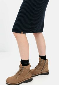 Tanfarbene Wildleder-Stiefeletten mit Schnürung vorne und seitlichem Reißverschluss, Gummisohle und leicht rosafarbenem Farbton, kombiniert mit einem marineblauen, gerippten Strickrock.