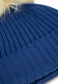 Blauwe ribgebreide wintermuts met omgevouwen rand en een beige nepbont pompon bovenop, close-up weergave.