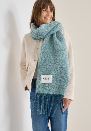 Niebiesko-skalny szalik w kratę wykonany z miękkiego materiału, z frędzlami na końcach i białą metką z napisem "CECIL ACCESSORIES". Nosi się go na lekką kurtkę.