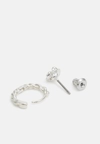 Zilveren ringoorbel met een gedraaide ontwerp, vergezeld van een studoorbel met een gestructureerde, abstracte vorm en een metalen stud.