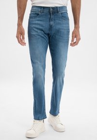 Jeans en denim bleu clair avec une coupe droite, design à cinq poches, légères décolorations et détails cousus. Associés à des baskets blanches.